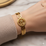 Medusa Aeterna Bracelet. Bold. Timeless. Captivating. This striking cuff features the iconic Medusa medallion centered between the legendary Greek Key motif. Crafted from durable stainless steel and richly plated in 21k gold.