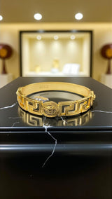 Medusa Aeterna Bracelet. Bold. Timeless. Captivating. This striking cuff features the iconic Medusa medallion centered between the legendary Greek Key motif. Crafted from durable stainless steel and richly plated in 21k gold.